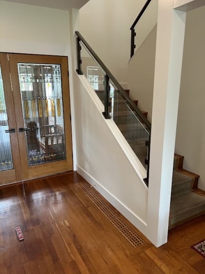 Black-post glass railing runs along a carpeted stair near leaded glass front doors.