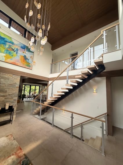 Floating oak stair with post-mounted glass railing in a great room with pendant lights and colorful art
