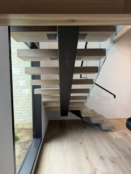 Black mono stringer with white oak floating treads and frameless glass beside a stone-clad window