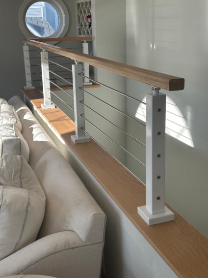 White posts with cable infill and a wood cap rail sit atop a half wall beside a living room sofa.