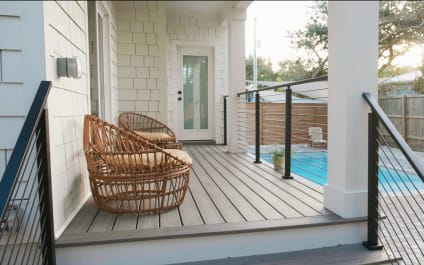 Black rod railing flanks steps from a white porch to a pool patio with wicker chairs.