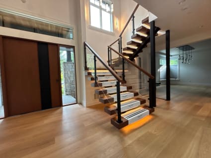 Walnut floating treads with Viewrail tread covers and under-tread LEDs on a mono stringer with glass and post railing in an entry.