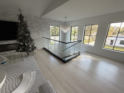 Frameless glass in a black base rail with a black cap guards a stair opening in a bright living room.