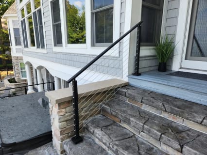 A black-post cable railing follows stone-veneer steps up to a gray-sided home.