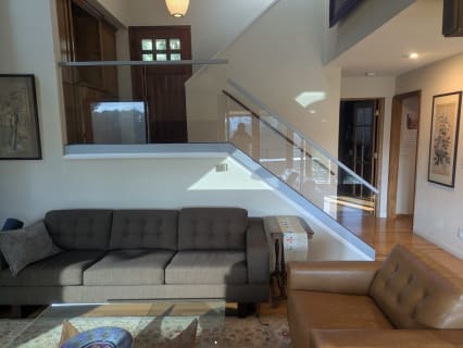 Frameless glass railings line a stair and upper landing in a bright living room.