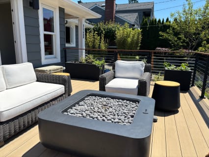 Black rod railing with a wood cap surrounds a composite deck with outdoor seating and a fire table.