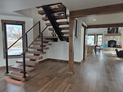 A black FLIGHT switchback with walnut treads, cable railing and LED base beside a timber post and mountain-view windows.