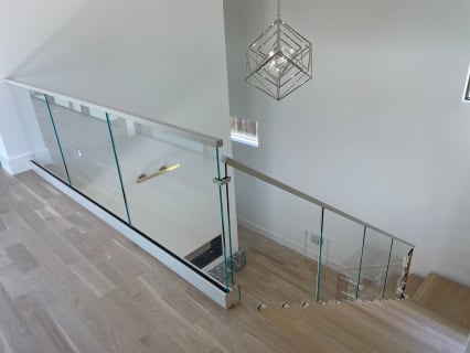 Frameless glass base rail railing with a slim handrail wraps a stair opening on white oak flooring.