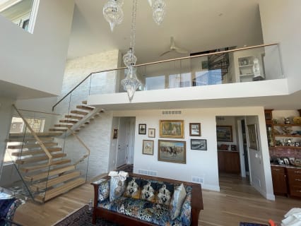 Light floating treads with glass railing and wood handrail rise to a glass-railed loft above a living room.