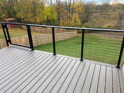 Black posts and top rail with cable infill along a gray composite deck overlooking a fenced lawn in autumn.