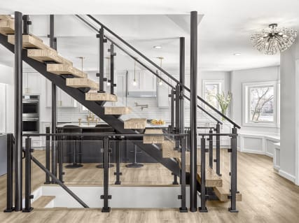 Thick light wood treads on black steel stringers with black post glass railing in a bright open kitchen.