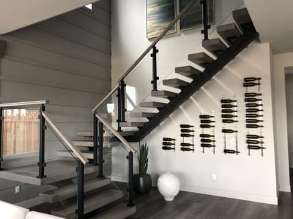 Open floating stair with gray treads and black posts holding glass panels beside a wall-mounted wine display.