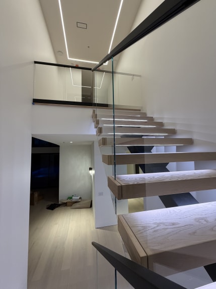 Oak floating treads with LED strips beside frameless glass and a linear light ceiling