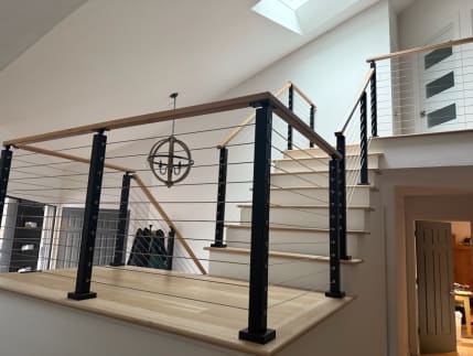 Black cable posts with white oak top rail guard a stair landing beneath a skylight and orb chandelier.