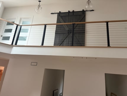 Black-post cable railing with a white oak cap lines a loft with a barn door above a hallway.