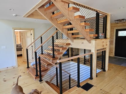 Open pine treads on wood stringers with black post cable railing around a switchback in a pine-floored cabin.