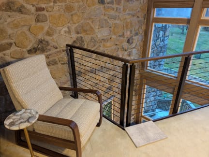 Black cable railing with a wood handrail guards a carpeted loft reading nook beside a fieldstone wall.