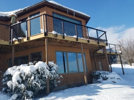 Black side-mounted cable railing on an elevated deck of a cedar home surrounded by fresh snow.