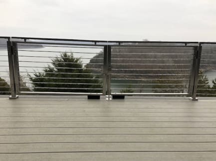 Stainless-framed cable double gate set into a cable railing on a gray deck above a lake.