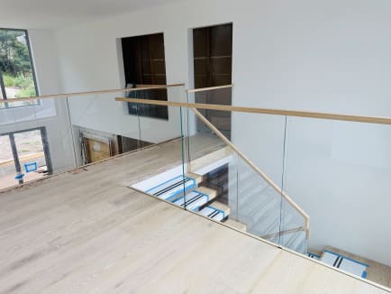 Frameless glass and wood handrail guard a stair opening, with floating treads below