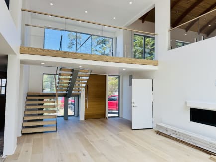 Double-height great room with a frameless glass loft railing and floating stair below