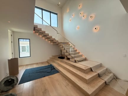 Connected white oak Stack treads with LED lighting and frameless glass beneath a wall of round sconces