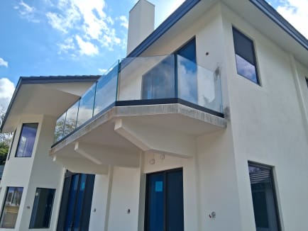 Angled frameless glass balcony on a dark base rail jutting from a white modern home