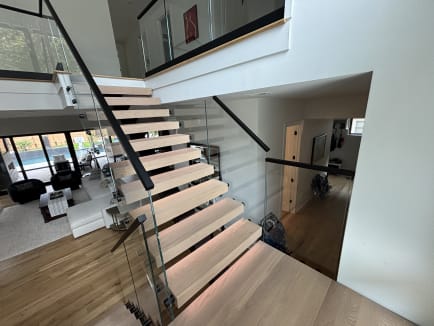 White oak floating stair with LED treads and frameless glass with a black cap overlooking a living room and pool