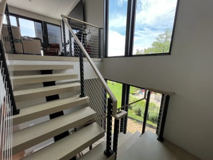 Pale oak floating treads with black cable railing rising toward a window over the lake