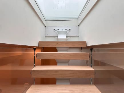 Head-on view of thick white oak floating treads between two frameless glass panels under a skylight