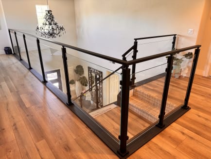 Black aluminum post glass railing wraps an upstairs loft and stair opening under a wrought-iron chandelier