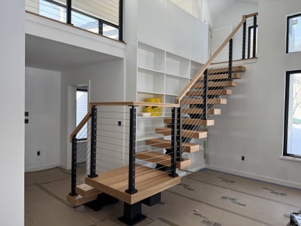 Red oak FLIGHT Mono with a floating landing on a single post, black cable railing and oak handrail in a white great room