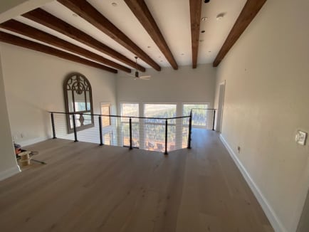 Black-post cable railing wraps a loft opening beneath dark timber beams with mountain views