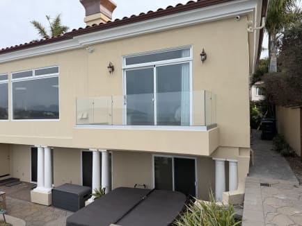 A frameless glass balcony railing on a stucco Mediterranean-style home above a stone patio.