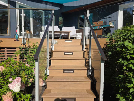 Post-to-post glass railing with dark handrails flanks lit composite deck stairs among hydrangeas.