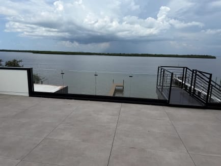 Frameless glass in a black base channel edges a tiled rooftop terrace overlooking a bay and boat dock.