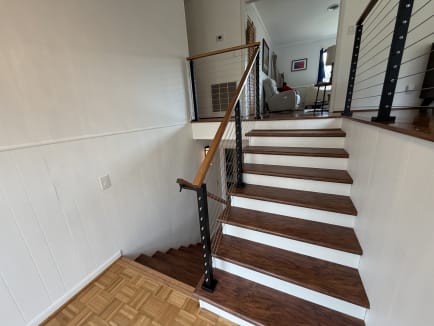 Black cable railing posts with a warm wood handrail line a split-level stair with white risers and cherry-toned treads.