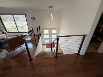 Black-post cable railing with wood handrail wraps a stair opening down to a bright entry with glass double doors.
