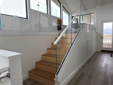 A frameless glass guard with white handrail lines an oak stair under a white vaulted ceiling.