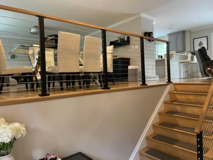 Black posts with cable infill and a wood cap rail separate a raised dining area from the stair.