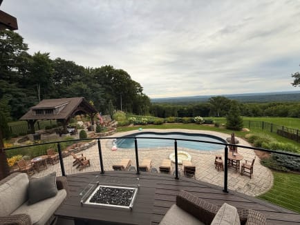 Curved composite deck with black cable railing and fire table overlooks a pool, pavilion and valley view.