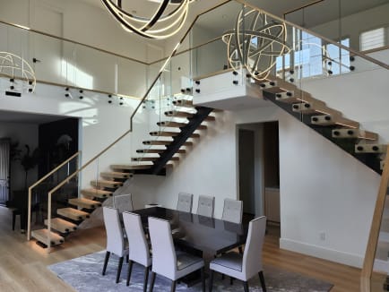 Black-stringer FLIGHT Mono stairs with oak treads and standoff-pin glass railing overlook a formal dining room.