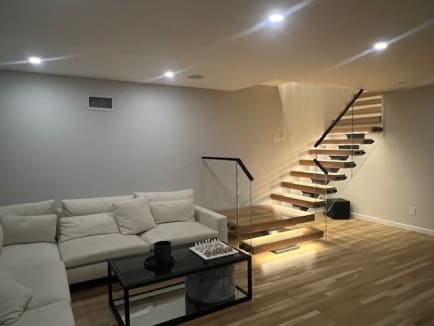 Floating oak treads with under-tread LEDs and glass railing rise from a cozy family room.
