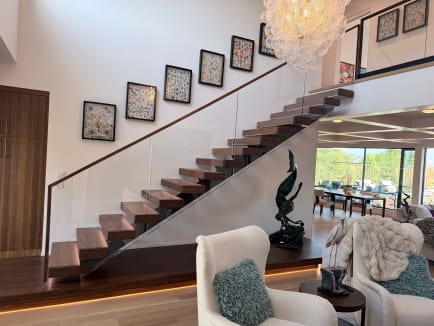 Walnut treads on a mono stringer rising from an LED-lit plinth beside frameless glass with a walnut handrail in a bright great room.