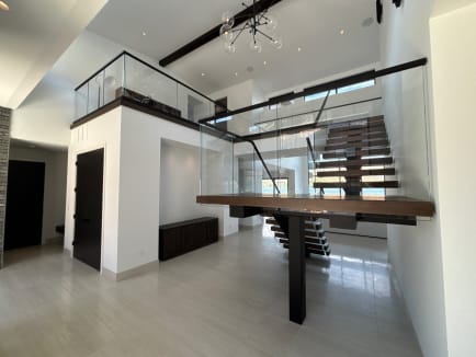 Dark wood floating treads on a black mono stringer switch back at a wood landing, framed by frameless glass on base rail in a bright double-height entry.