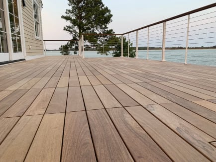 White-post cable railing with a wood cap edges a hardwood tile deck overlooking a bay.