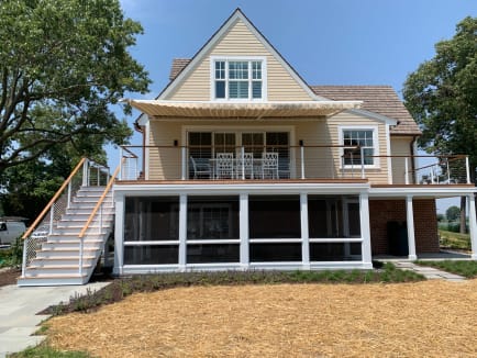 White-post cable railing with wood handrails lines the exterior stair and upper deck of a shingled waterfront cottage.