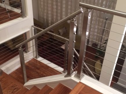 Brushed stainless posts and round handrail with cable infill follow a wood stair turning at a landing.