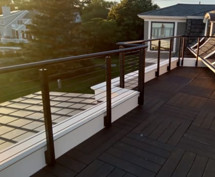 Bronze side-mount rod railing with round handrail around a dark rooftop deck at sunset.