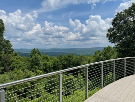 A curved composite deck edged with stainless posts, round handrail and cable infill overlooking forested hills.